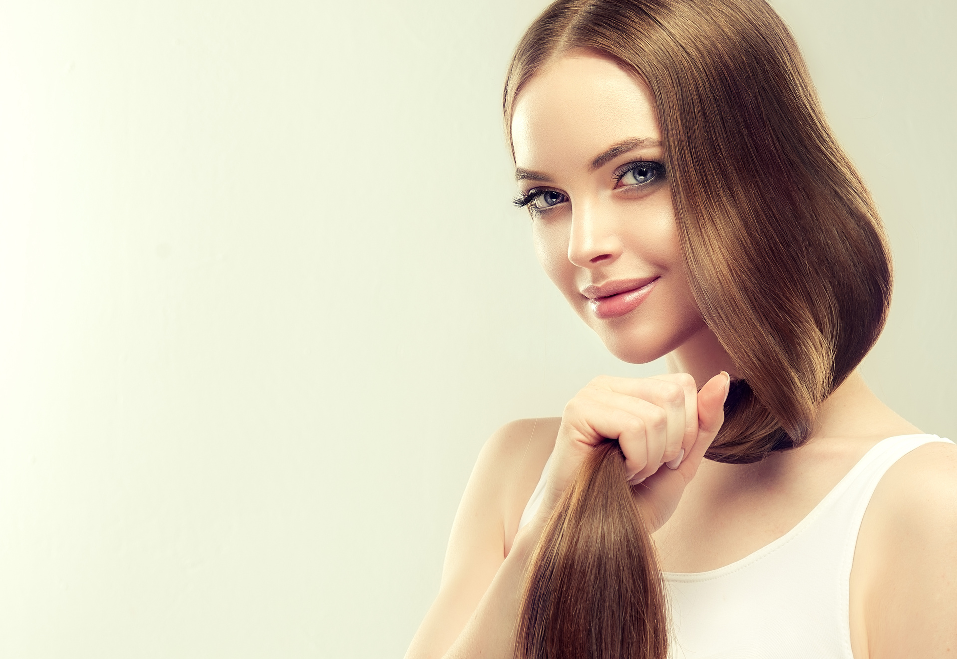 Young, brown haired beautiful model with long,  straight hair is holding tail of well groomed and healthy hair in the hand.
